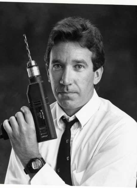 Tim Allen holding a drill in front of his face.