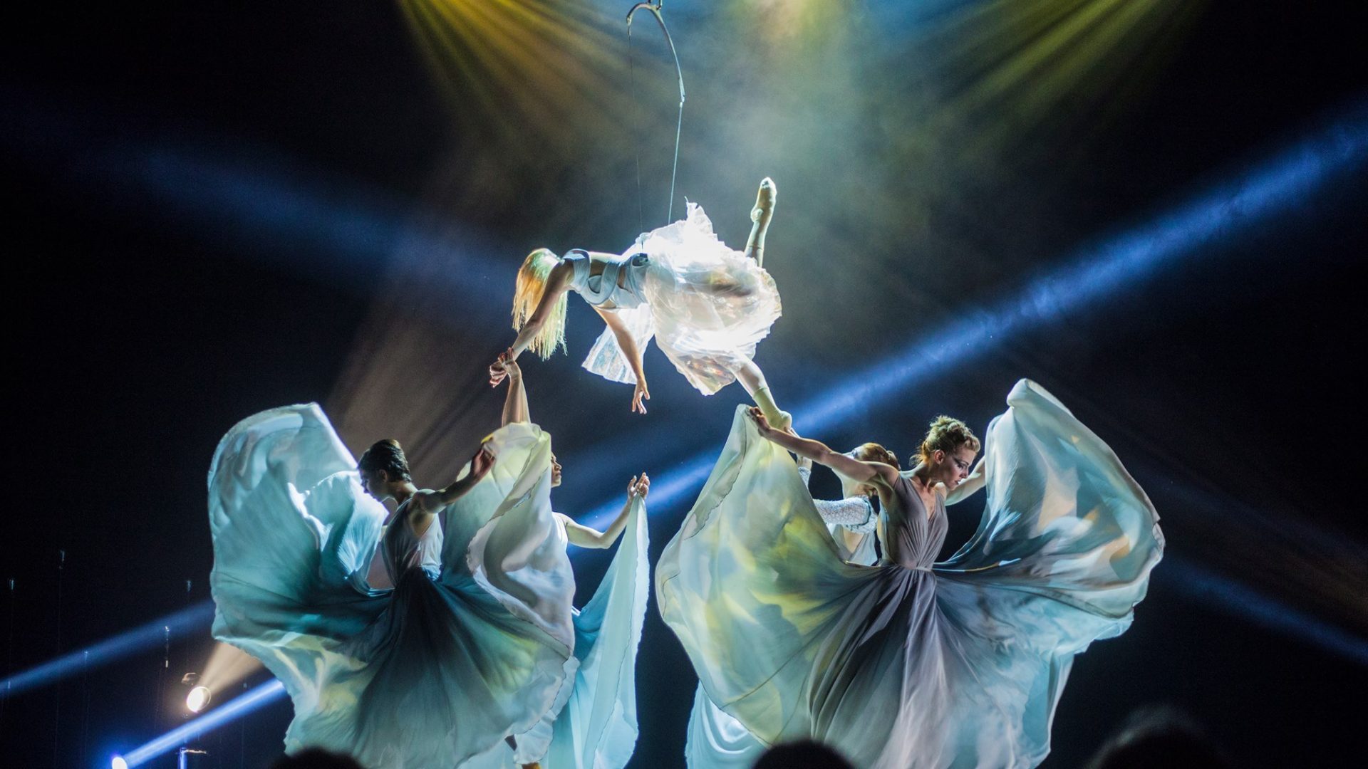 Three dancers from Quixotic suspended from the ceiling holding hands.